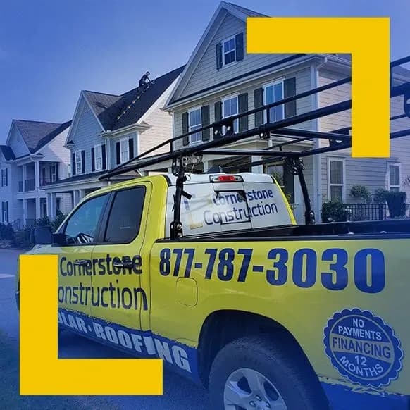 A Cornerstone Construction truck parked outside a row of homes. A worker works on a roof in the background.