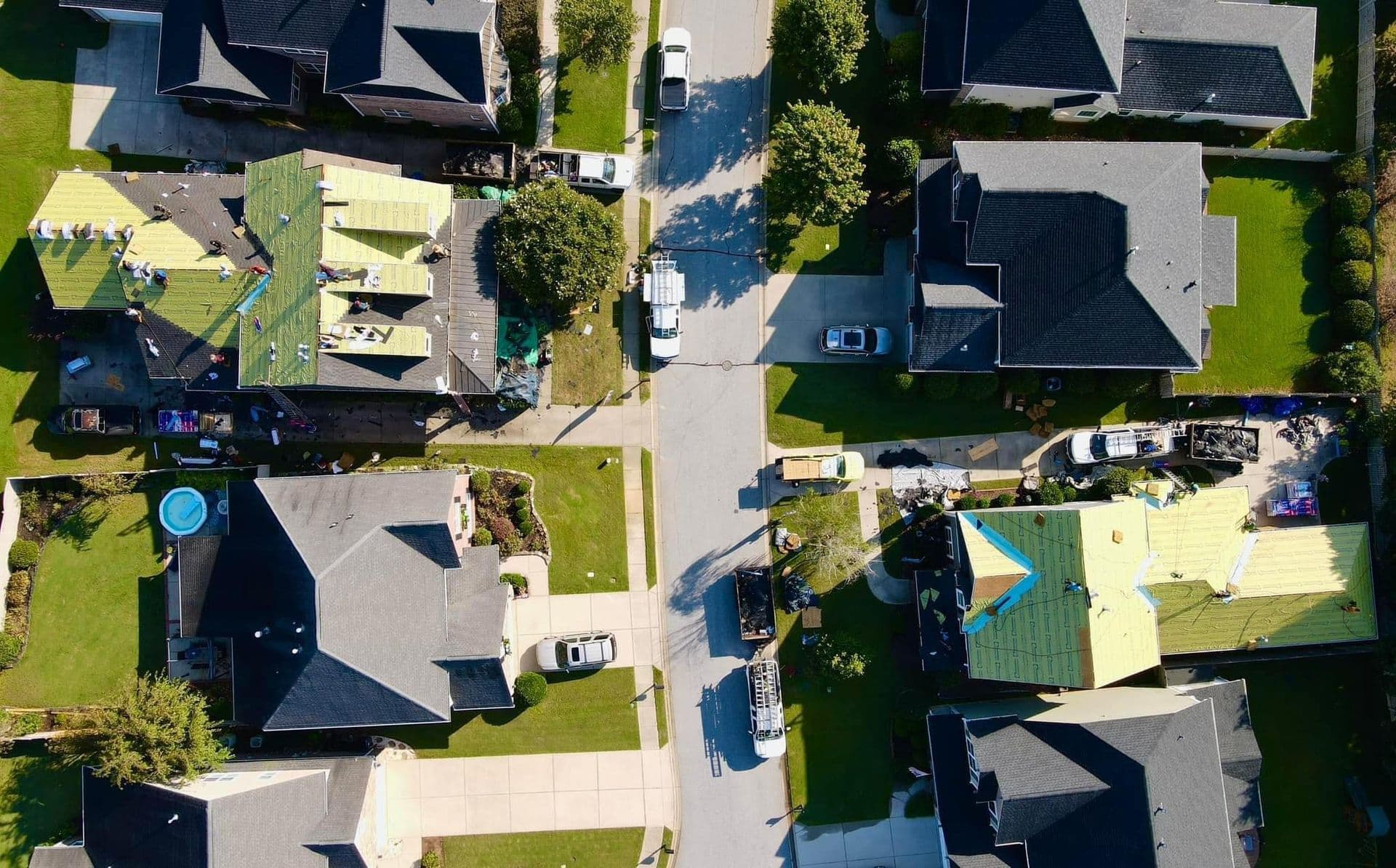 An overhead aerial view of a neighborhood. Two houses are having their roofs replaced.