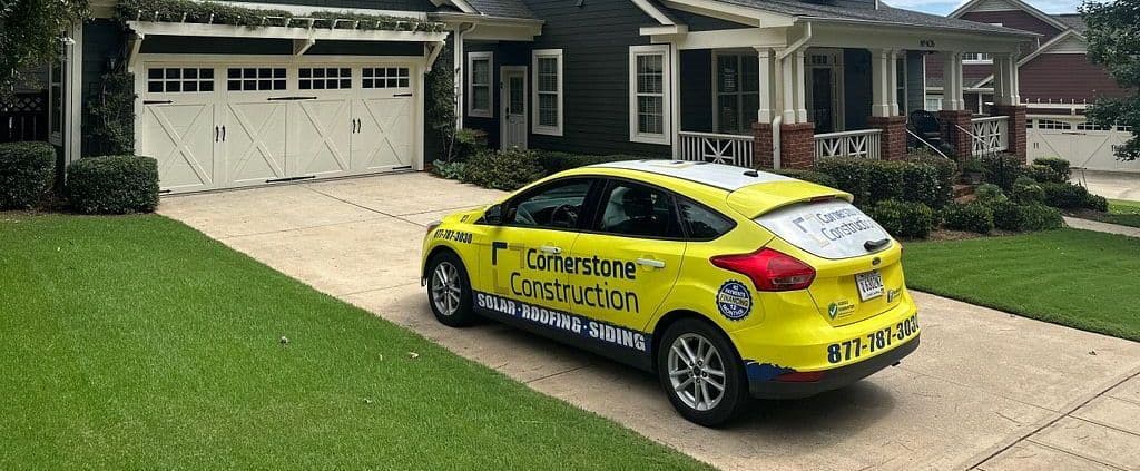 A yellow Cornerstone Construction car parked outside a dark house with white trim.