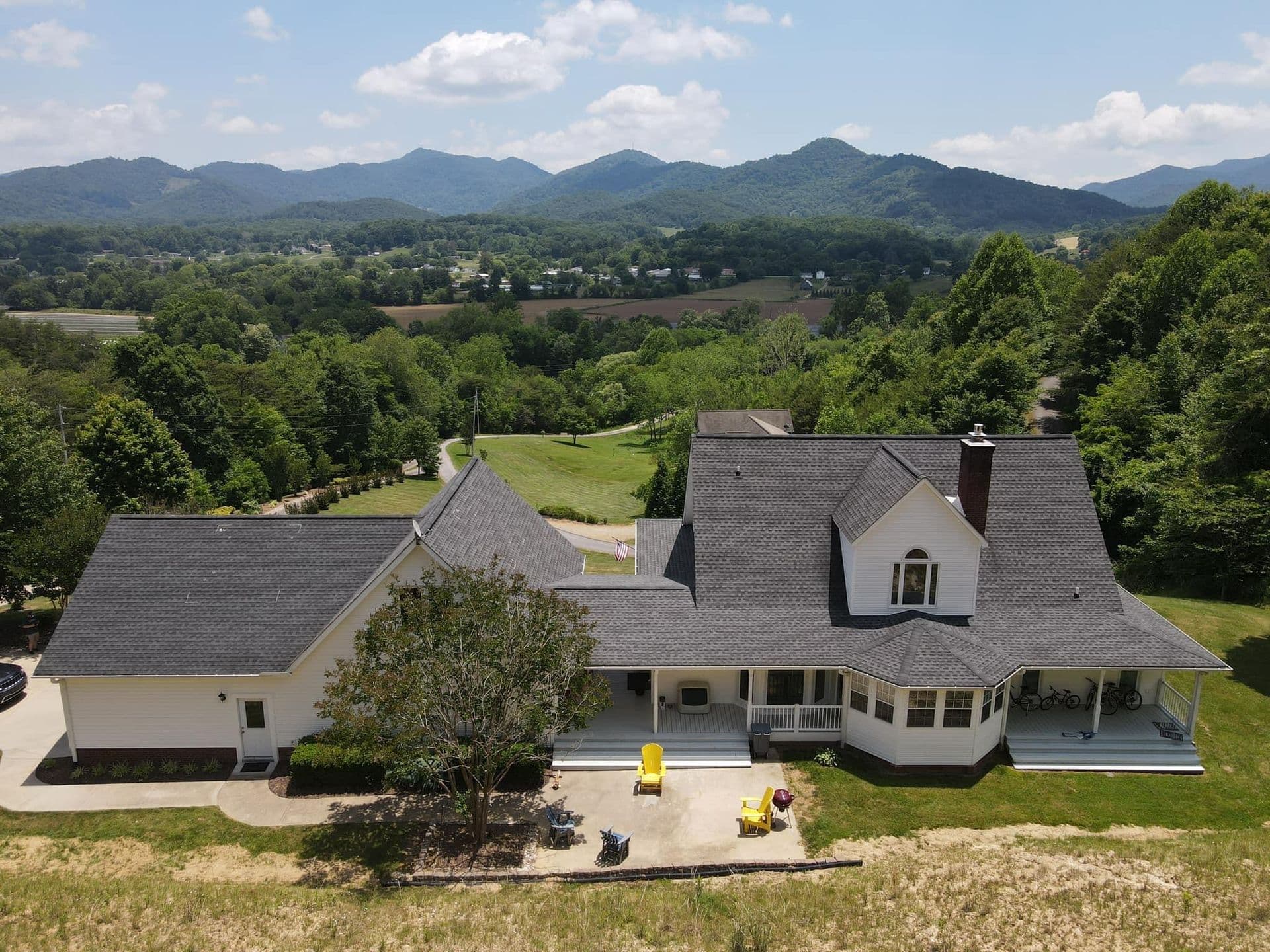 An aerial view of a large white house with new gray asphalt roofing.